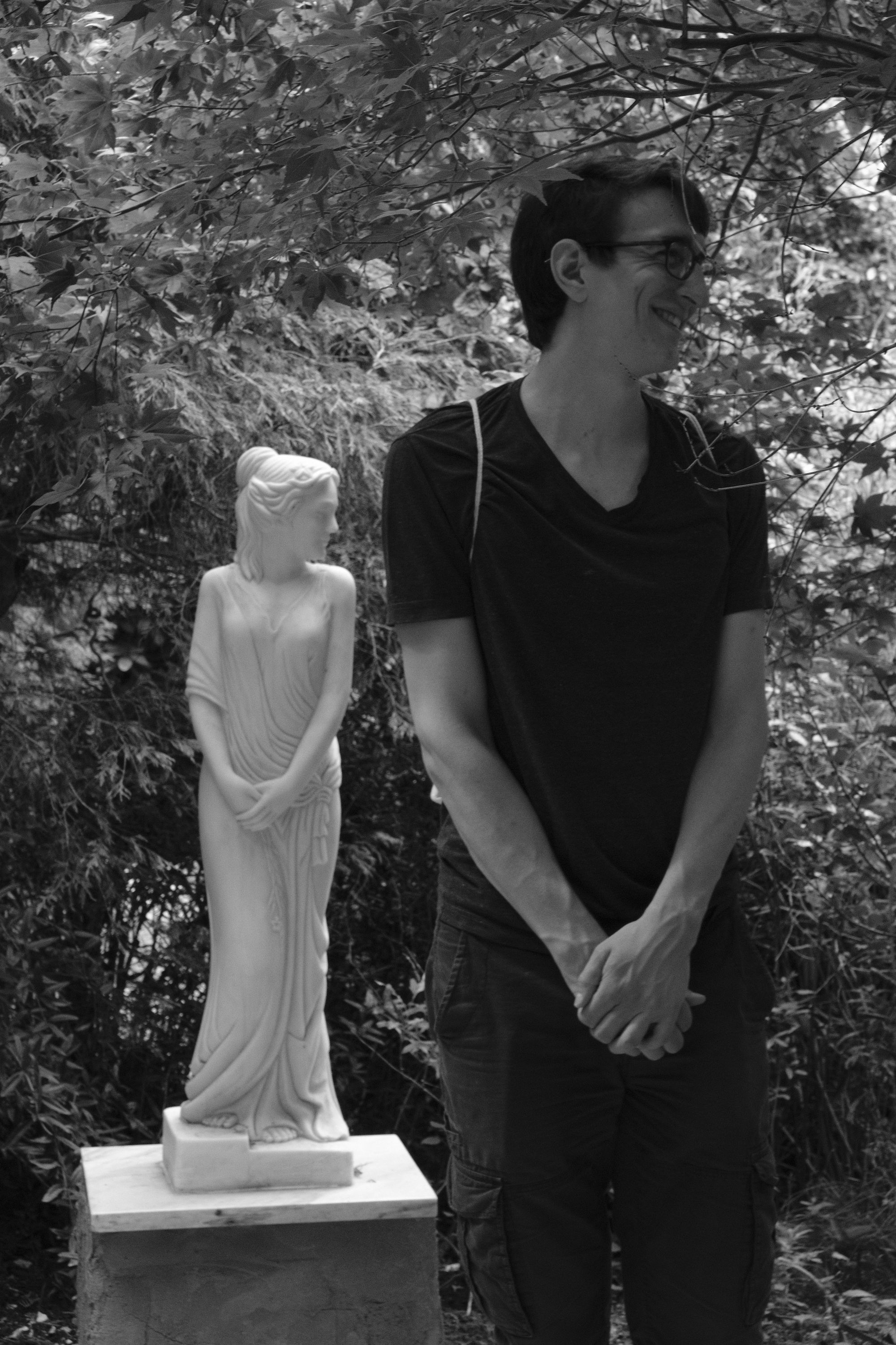 Young man surrounded by nature - imitates the pose of the statue behind him.